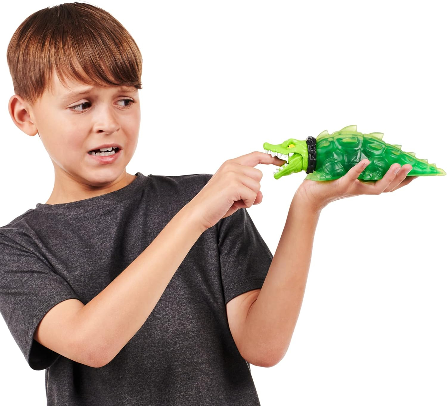 Un niño sosteniendo un juguete de cocodrilo verde. Su dedo cerca de su boca.