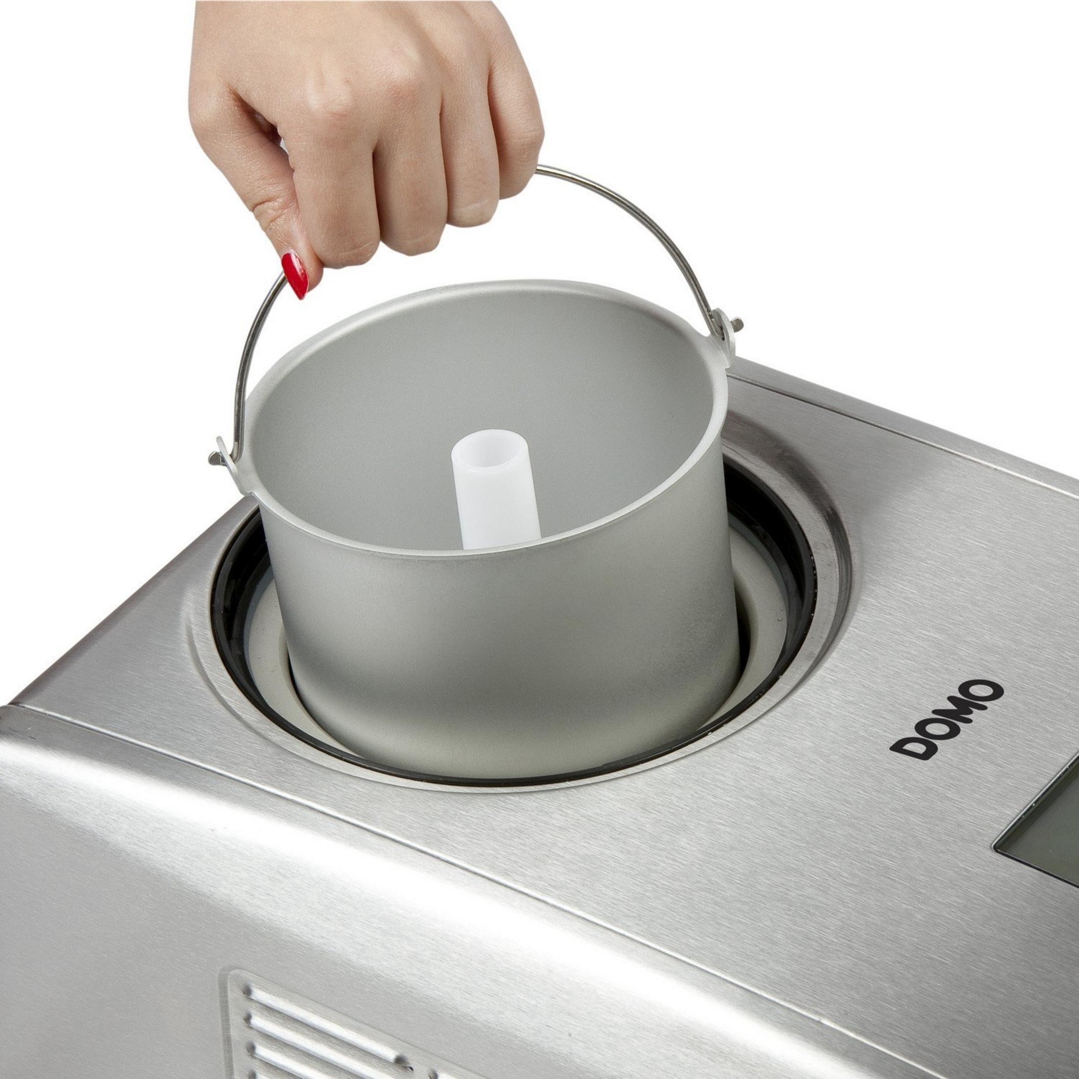 Une main soulève un bol argenté de sorbetière avec insert blanc d'une machine à glace argentée.