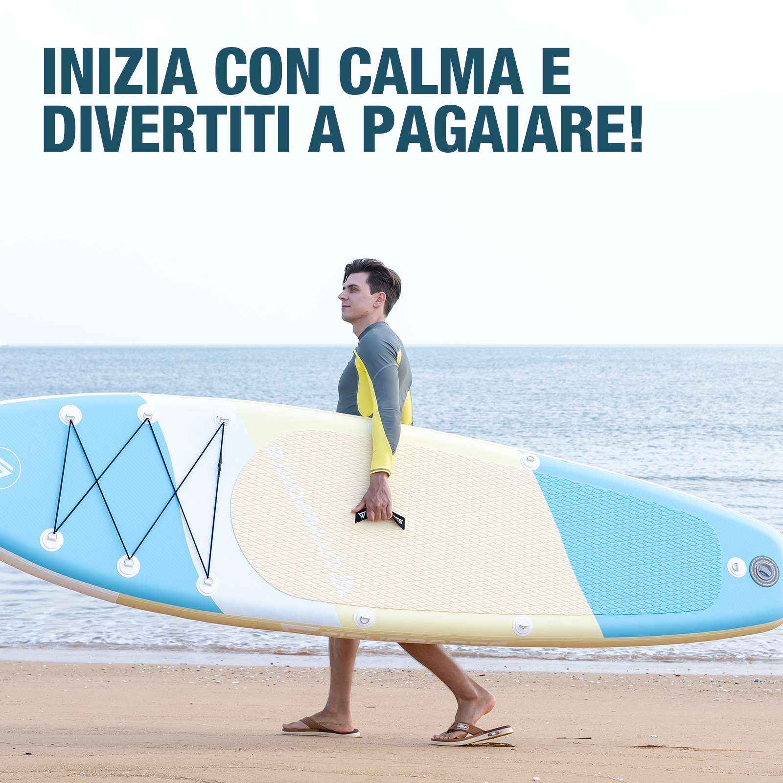 Uomo in muta porta tavola SUP su spiaggia, mare sullo sfondo.