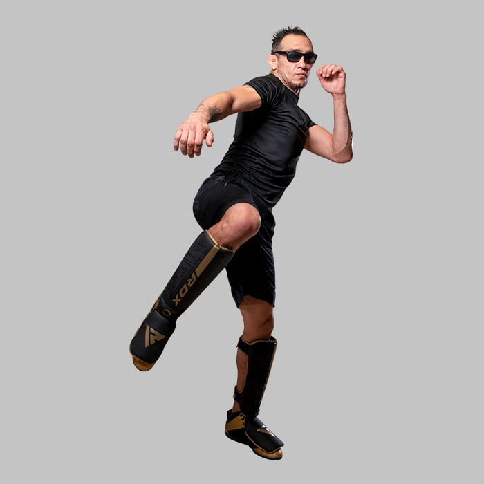 A man in black, wearing sunglasses and shin guards, is jumping.