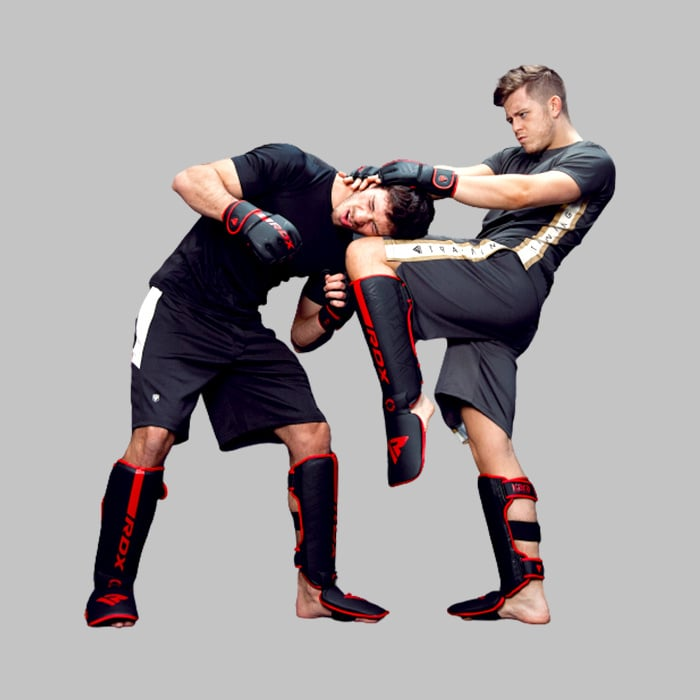 Two men in black fighting gear spar, one kicks the other's head.