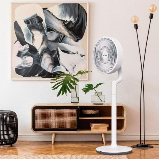 Un ventilatore da terra bianco è accanto a un mobile in legno con opere d'arte.