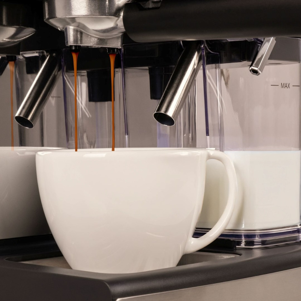 L'espresso cola da una macchina del caffè in una tazza bianca con latte sullo sfondo.