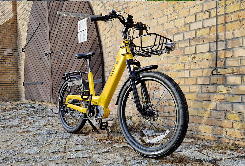 Ein gelbes Fahrrad mit Korb steht vor einer Ziegelwand und Holztür.