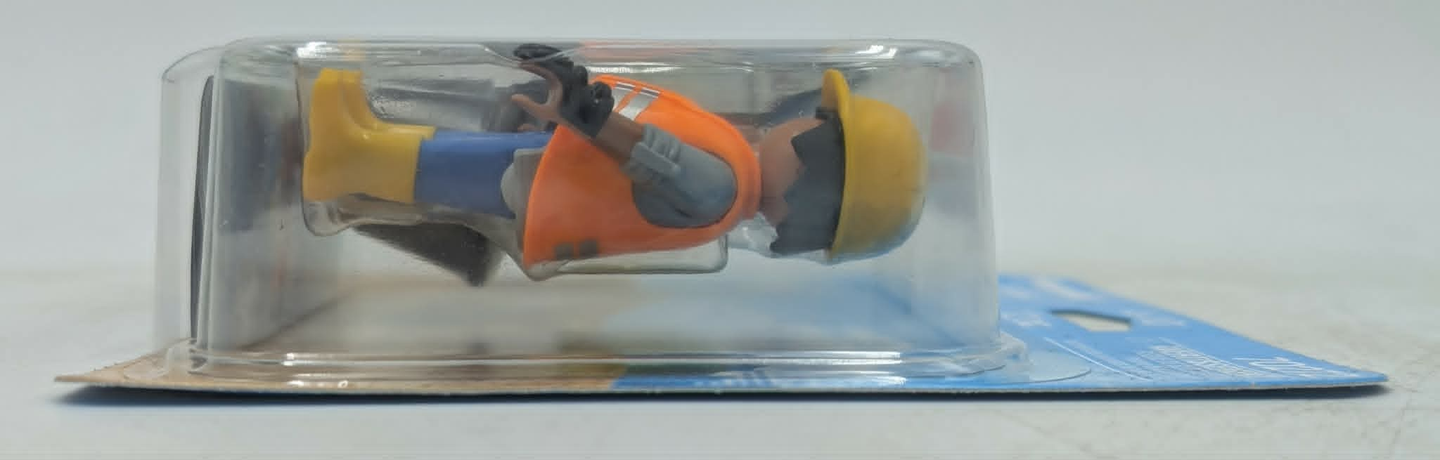 Ein Bauarbeiter-Spielzeug in gelben Stiefeln, blauer Hose, orangefarbener Weste und gelbem Helm in Blisterverpackung.