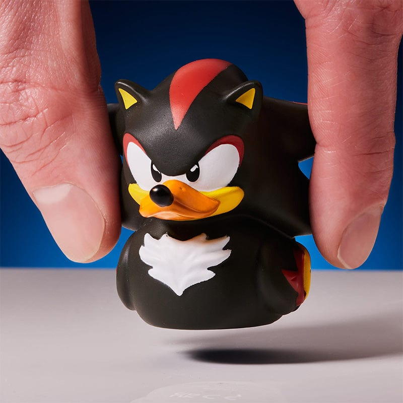 Schwarze Figur mit rotem Streifen am Kopf, gehalten von Fingern.