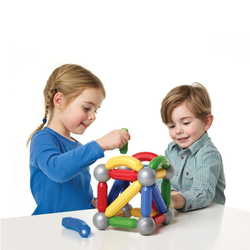 Zwei Kinder bauen mit bunten Magnetstäben und Kugeln auf einem Tisch.
