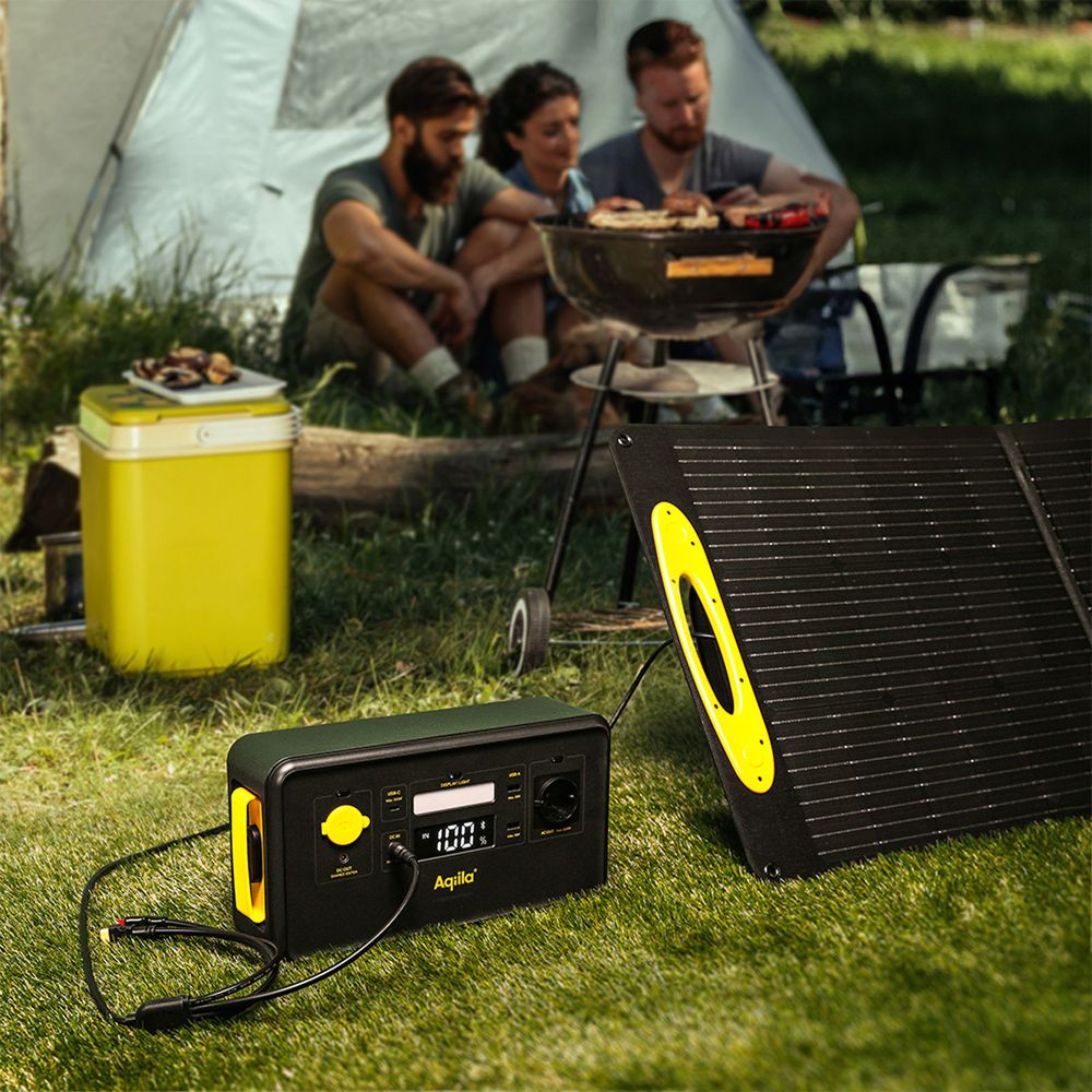 Drei Personen grillen draußen neben einem Solarmodul und einer Kühlbox.