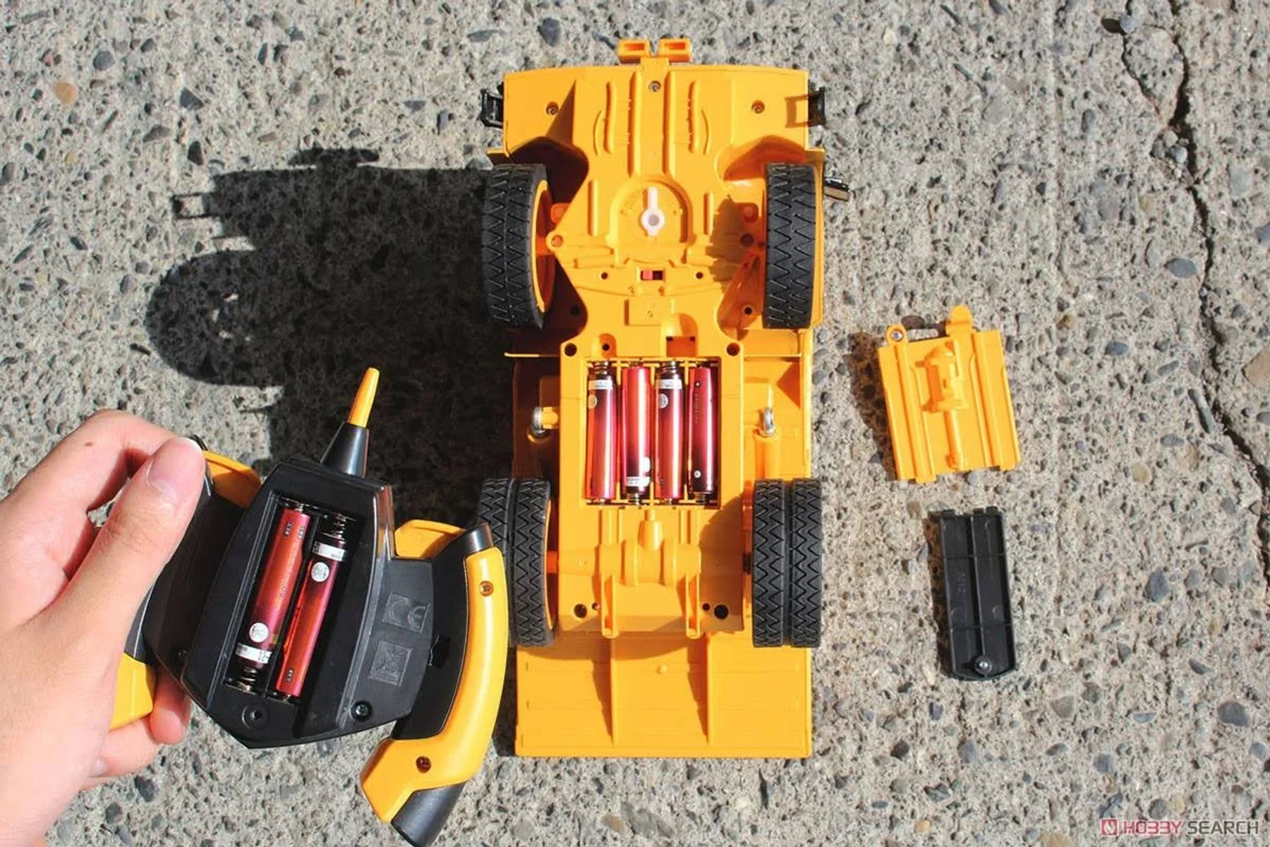 Gelbes ferngesteuertes Auto mit Batteriefach offen auf Beton.