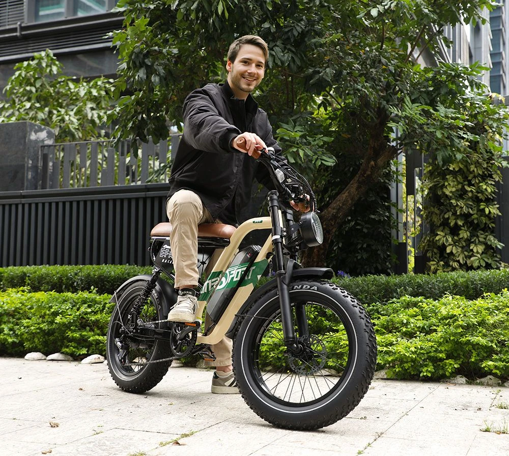 Un uomo siede su una bici elettrica beige all'aperto, circondato da piante verdi.