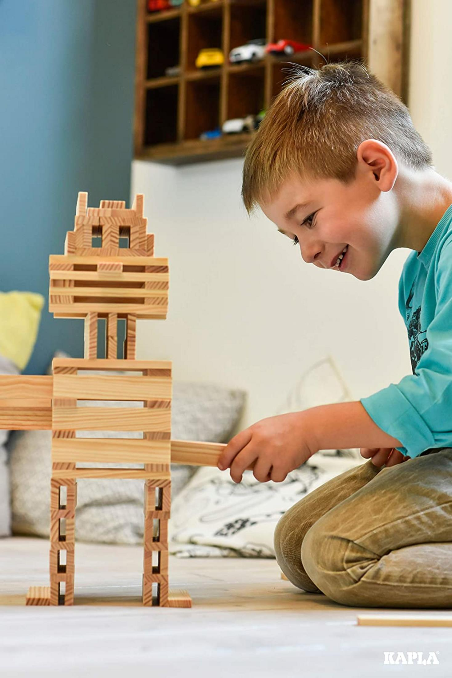 Ein Junge spielt mit Holzbausteinen und baut eine Figur. Er sitzt auf dem Boden.