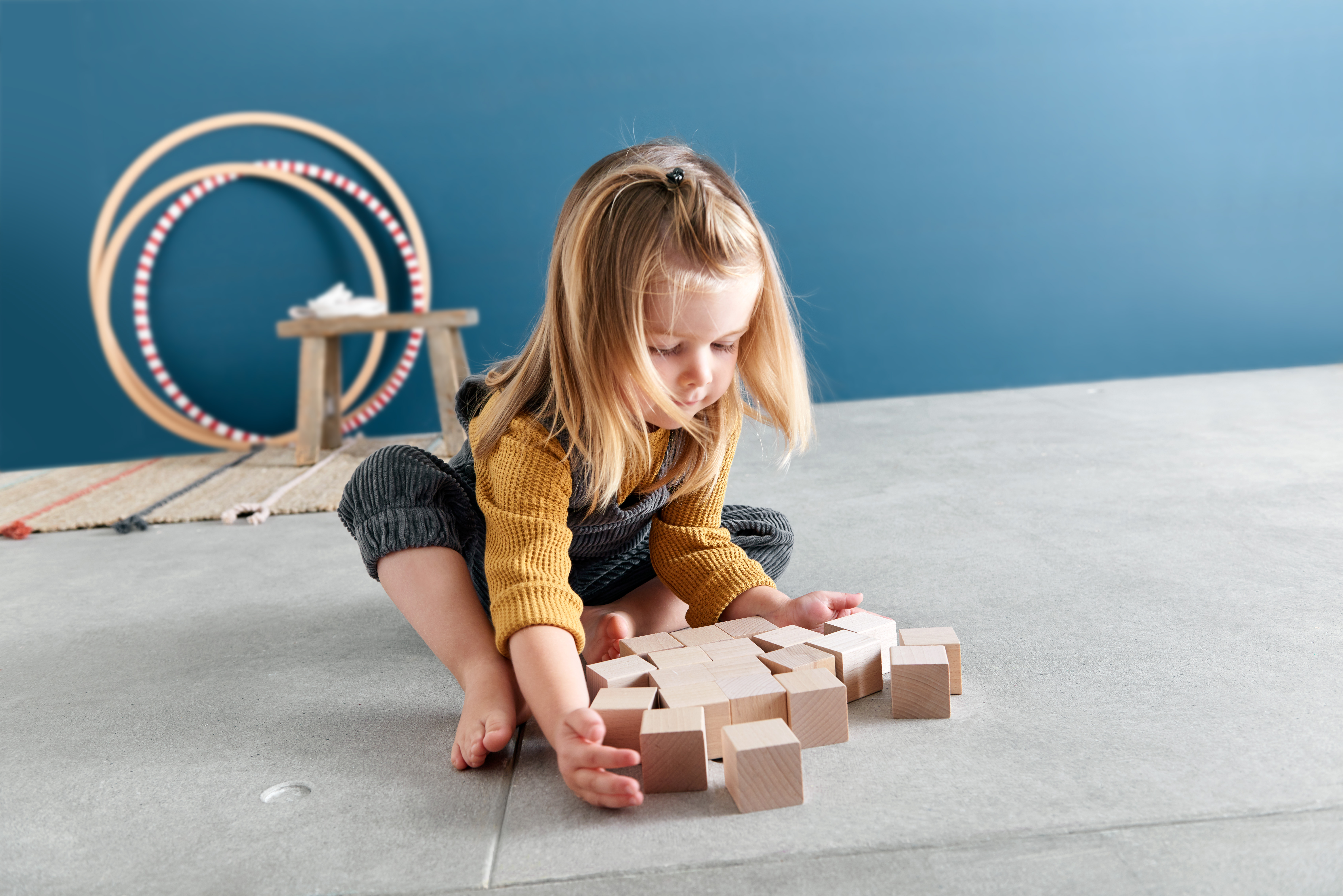 Bambina gioca con blocchi di legno su pavimento grigio.