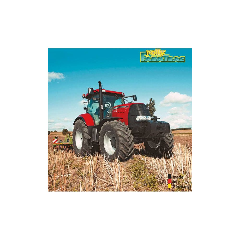 Ein roter Traktor steht auf einem Feld mit Strohresten unter blauem Himmel.