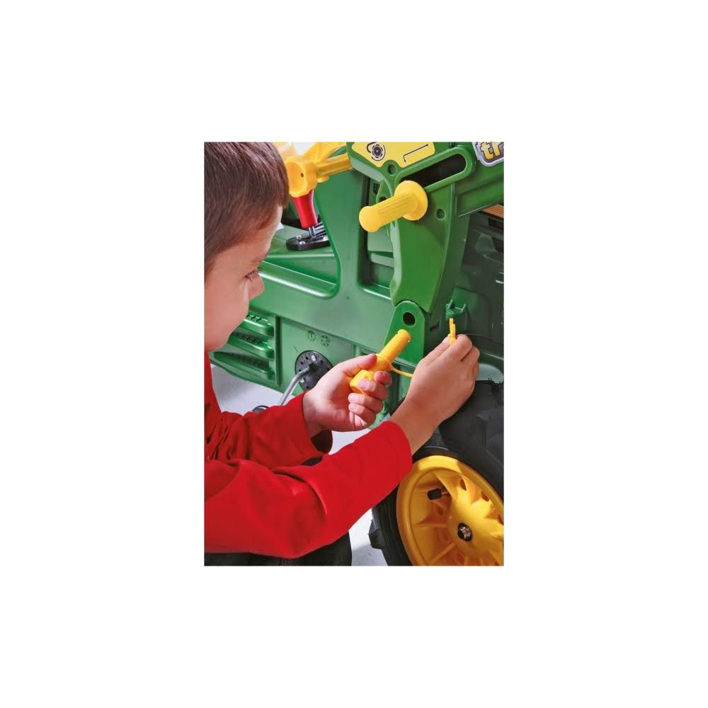 Ein Junge in einem roten Hemd repariert einen grünen Spielzeugtraktor mit einem gelben Werkzeug.
