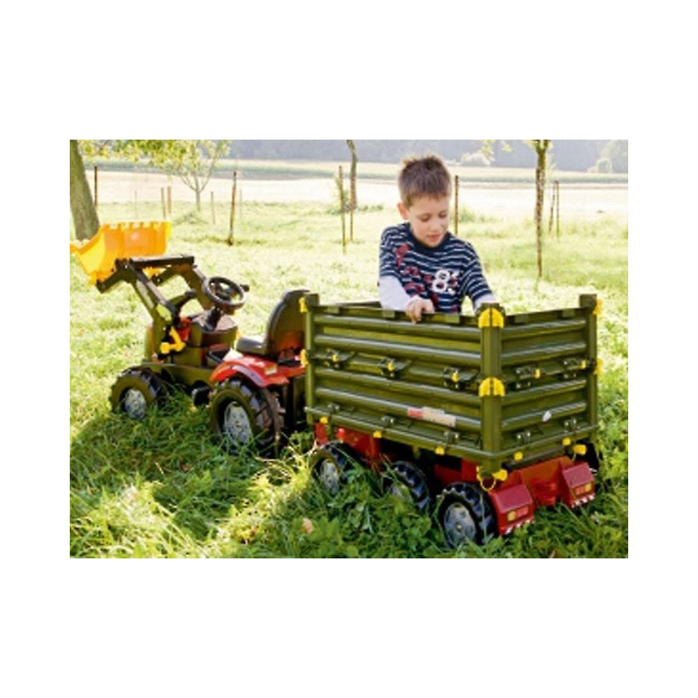 Un garçon joue avec un tracteur et une remorque jouets dehors dans l'herbe.