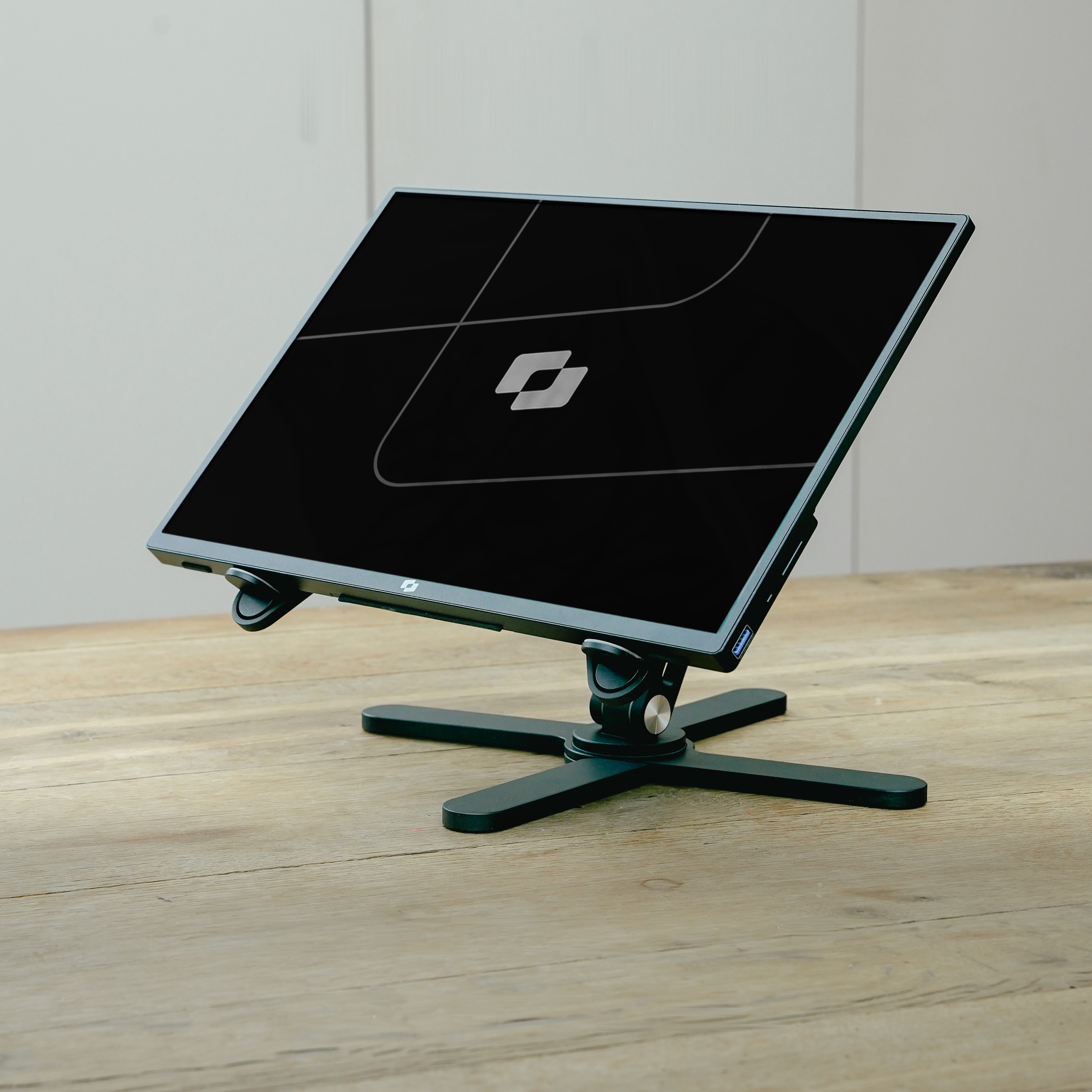 A black laptop stand holding a laptop, set on a wooden table.
