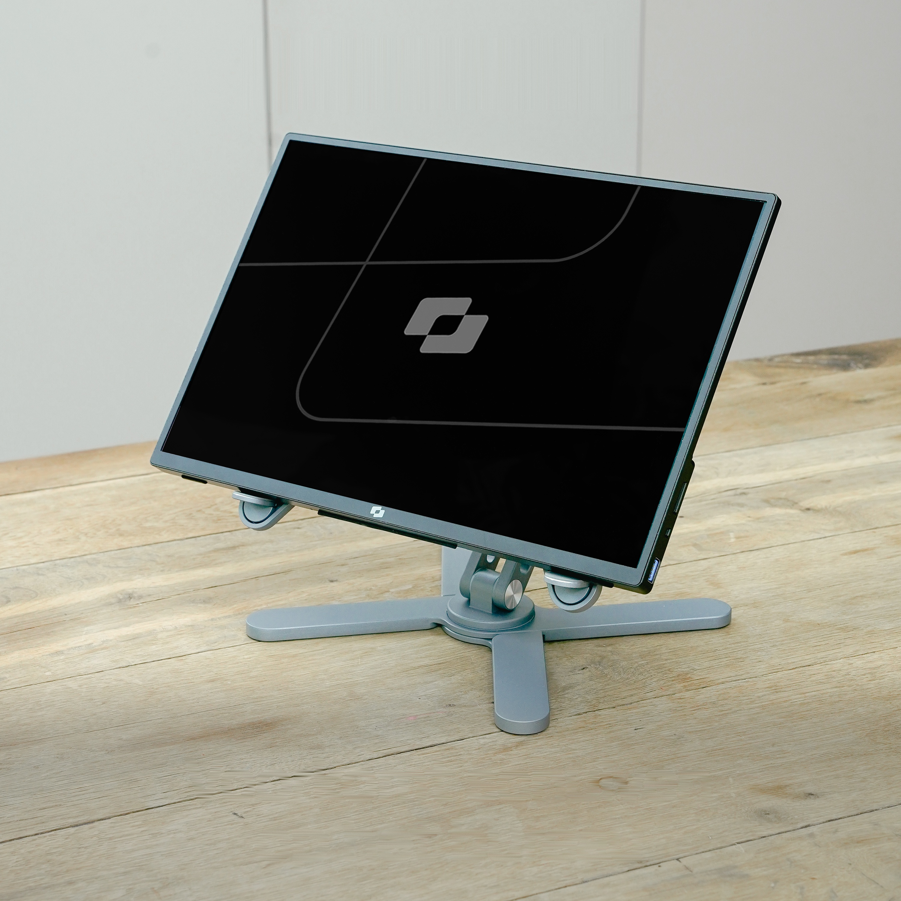 A gray monitor on an adjustable stand rests on a wooden table.