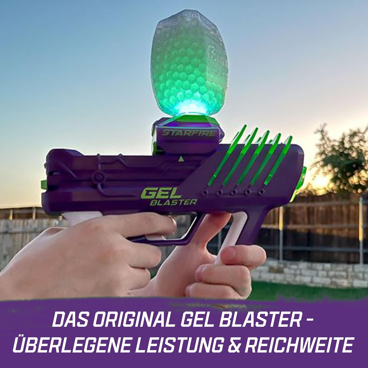 Lila Gel-Blaster mit grünem Magazin, gehalten von Händen, draußen bei Sonnenuntergang.