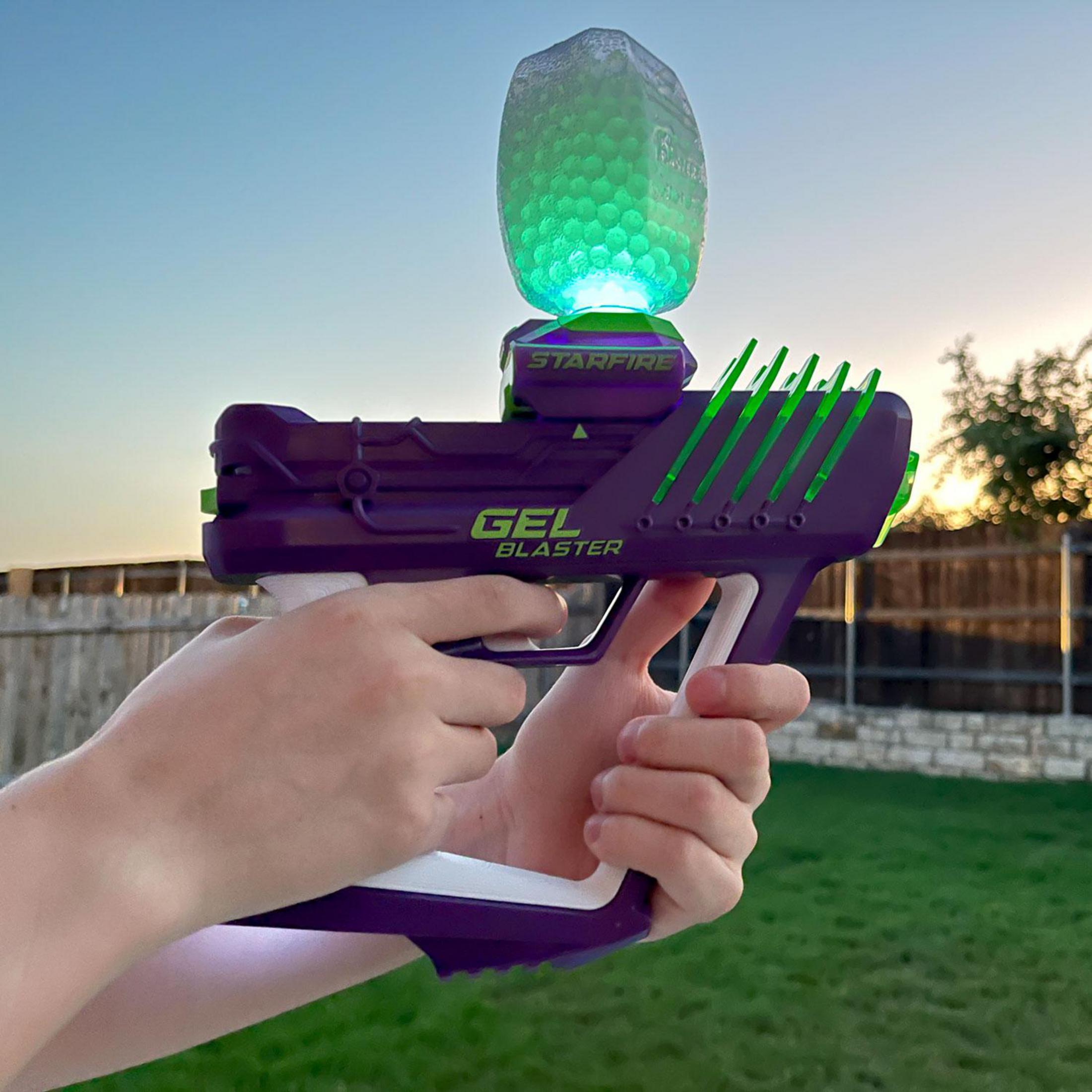 Eine Person hält eine lila und weiße Gel-Blaster-Waffe mit einem leuchtend grünen Magazin.