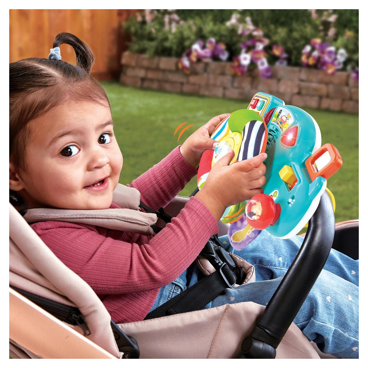 Un bambino felice è seduto in un passeggino, giocando con un volante giocattolo colorato all'aperto.