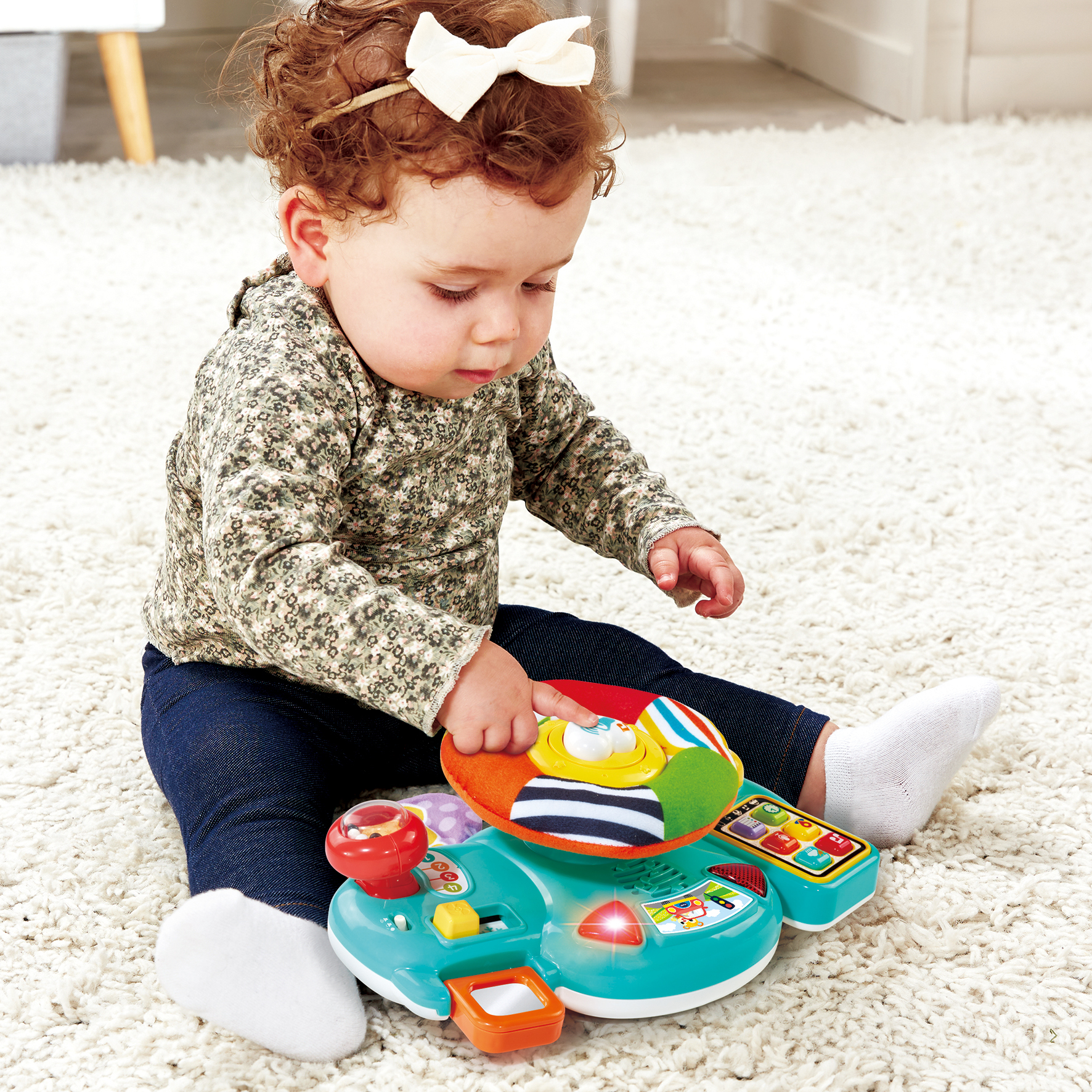 Bambina con riccioli rossi gioca con un giocattolo colorato su un tappeto.