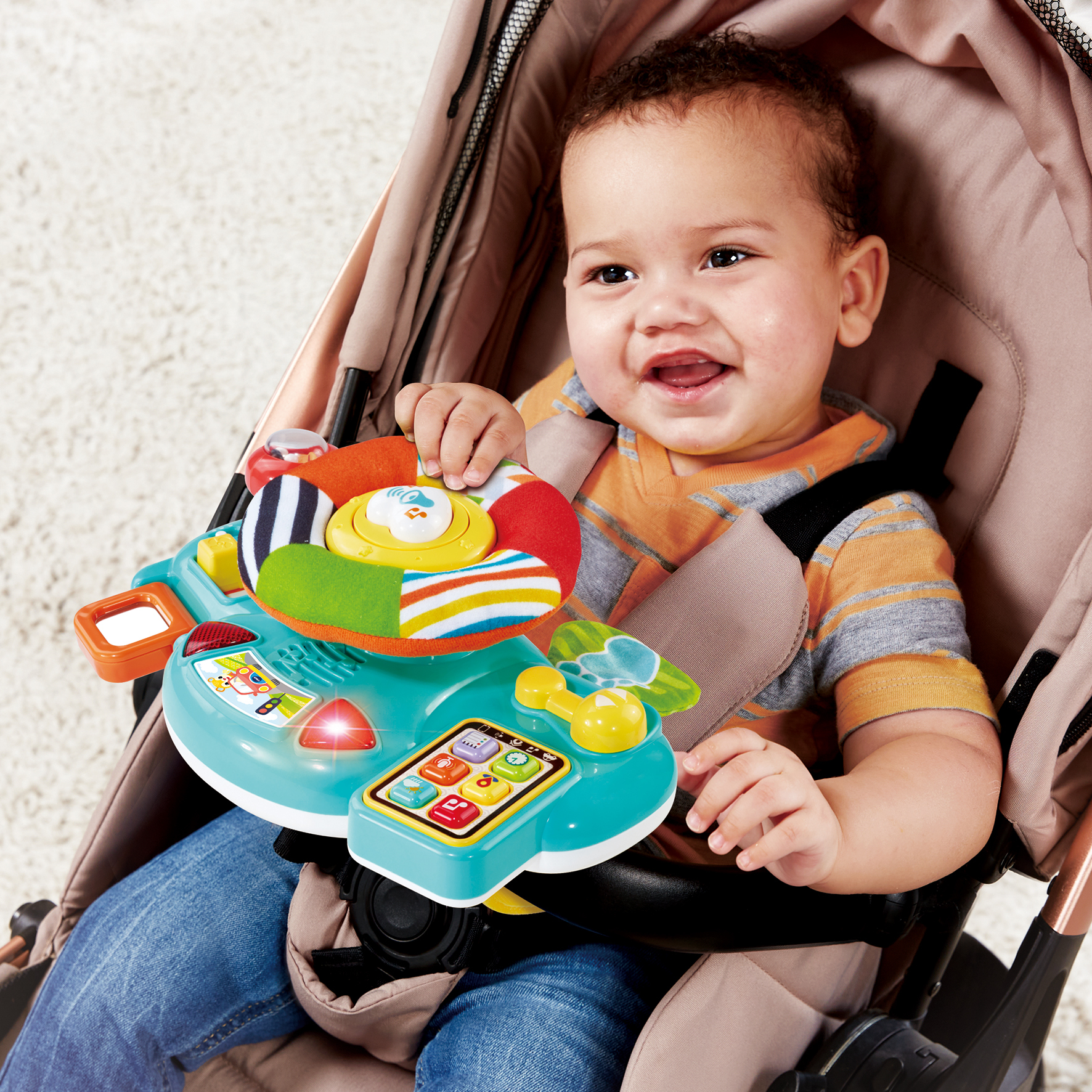 Un bambino seduto in un passeggino gioca con un volante giocattolo colorato.