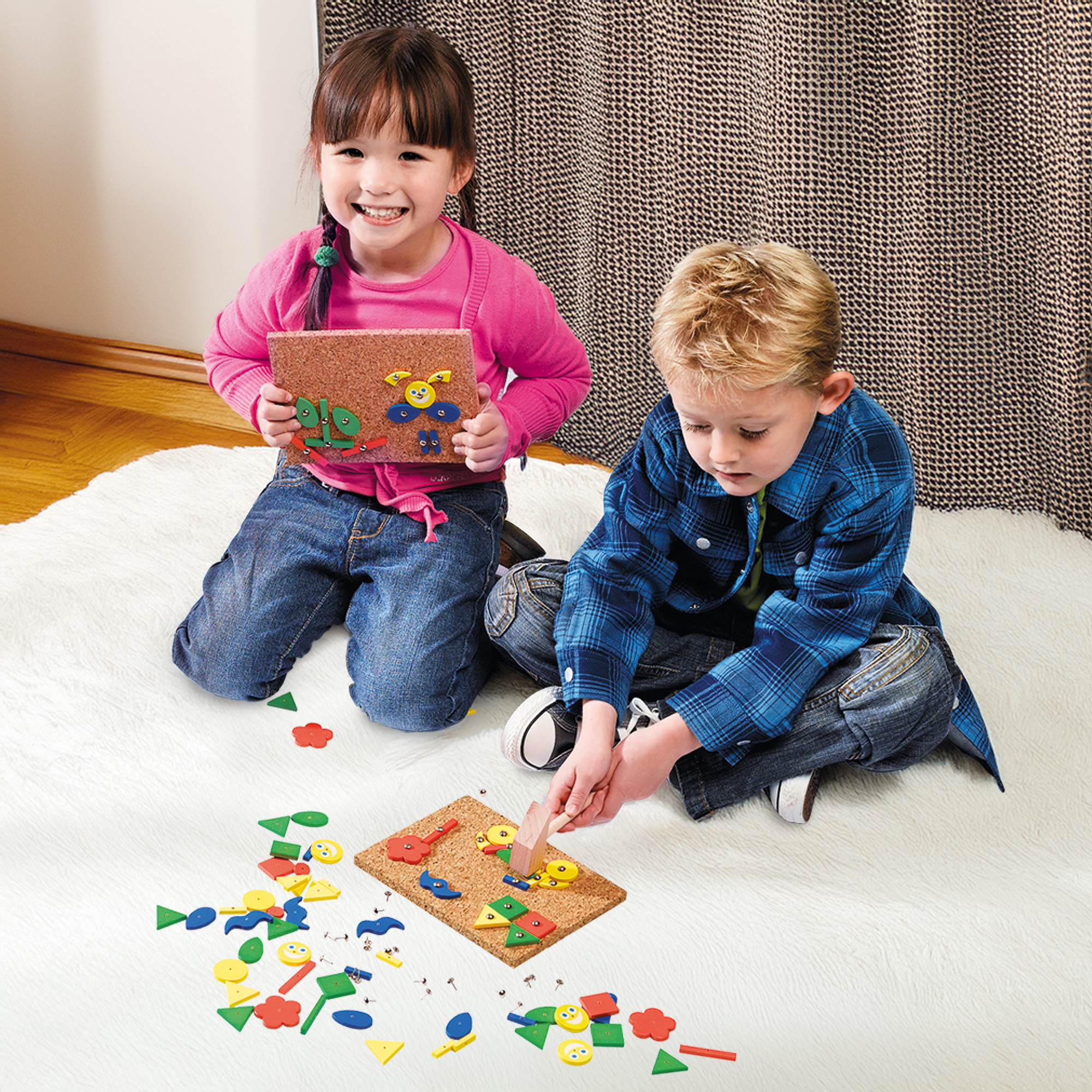 Zwei Kinder sitzen auf einem Teppich und basteln mit bunten Formen.