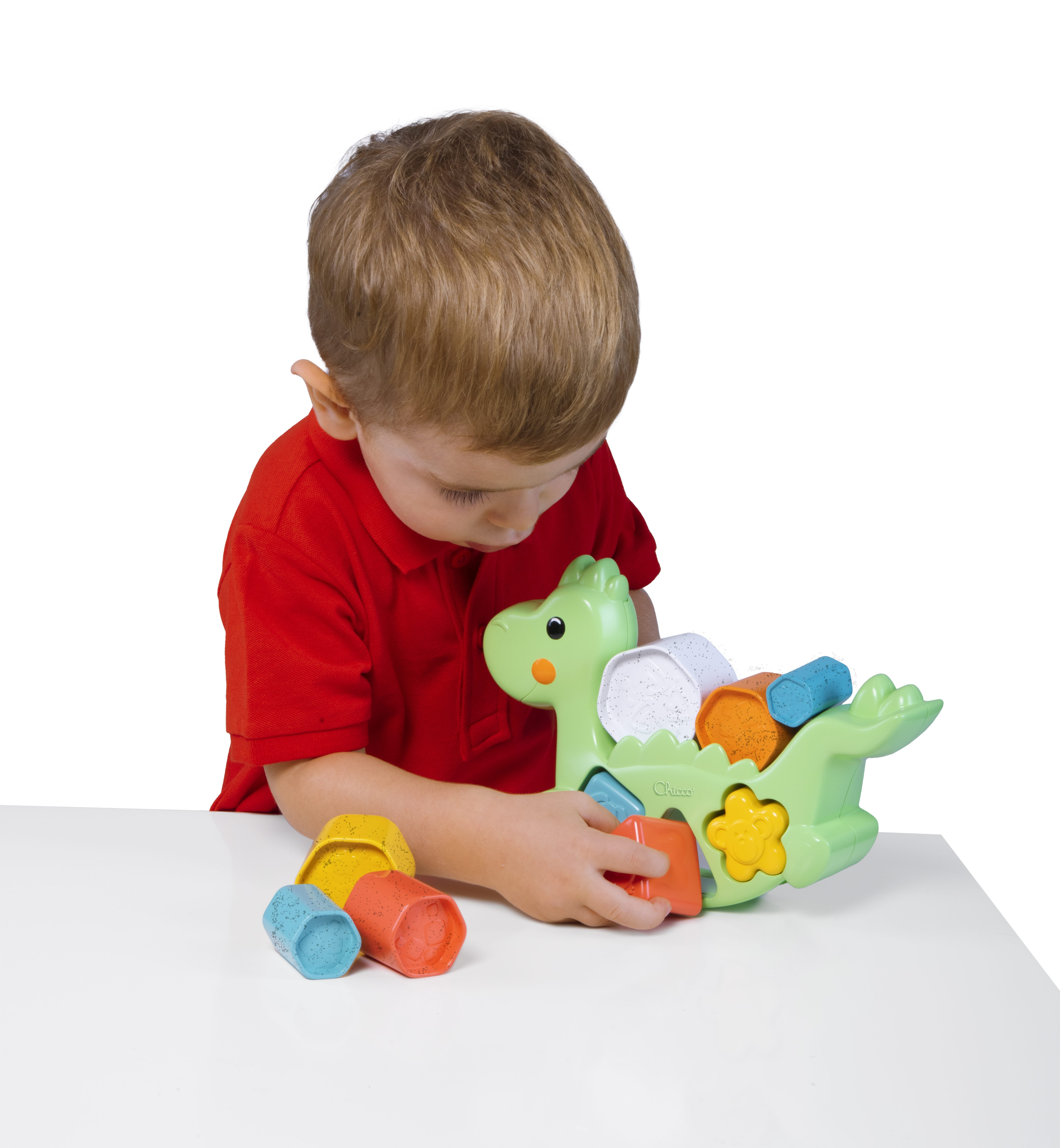 Ein Junge in einem roten Hemd spielt mit einem grünen Dinosaurier-Sortierspielzeug.