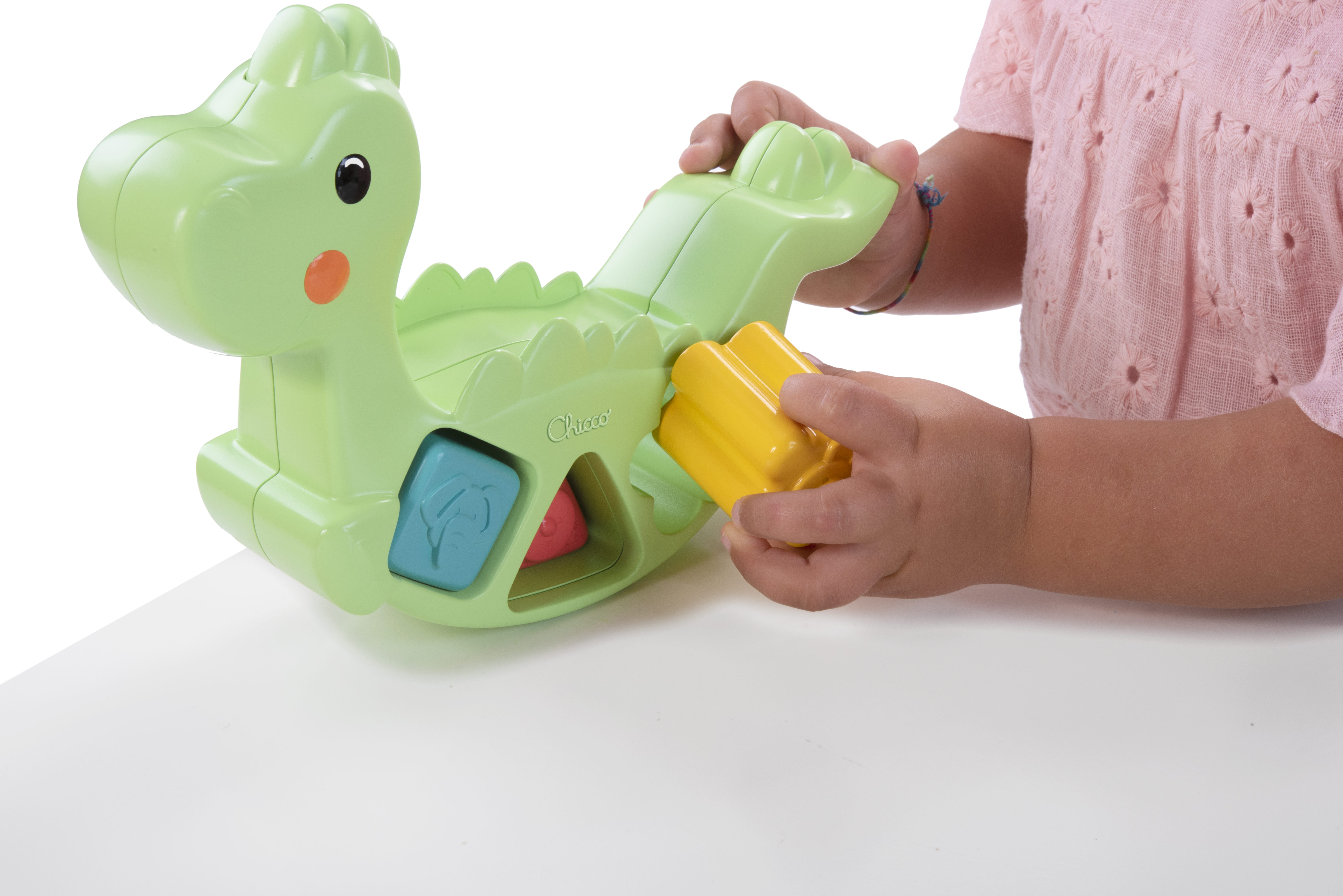 Ein Kind spielt mit einem hellgrünen Dino-Wipptier und gelben Bausteinen.