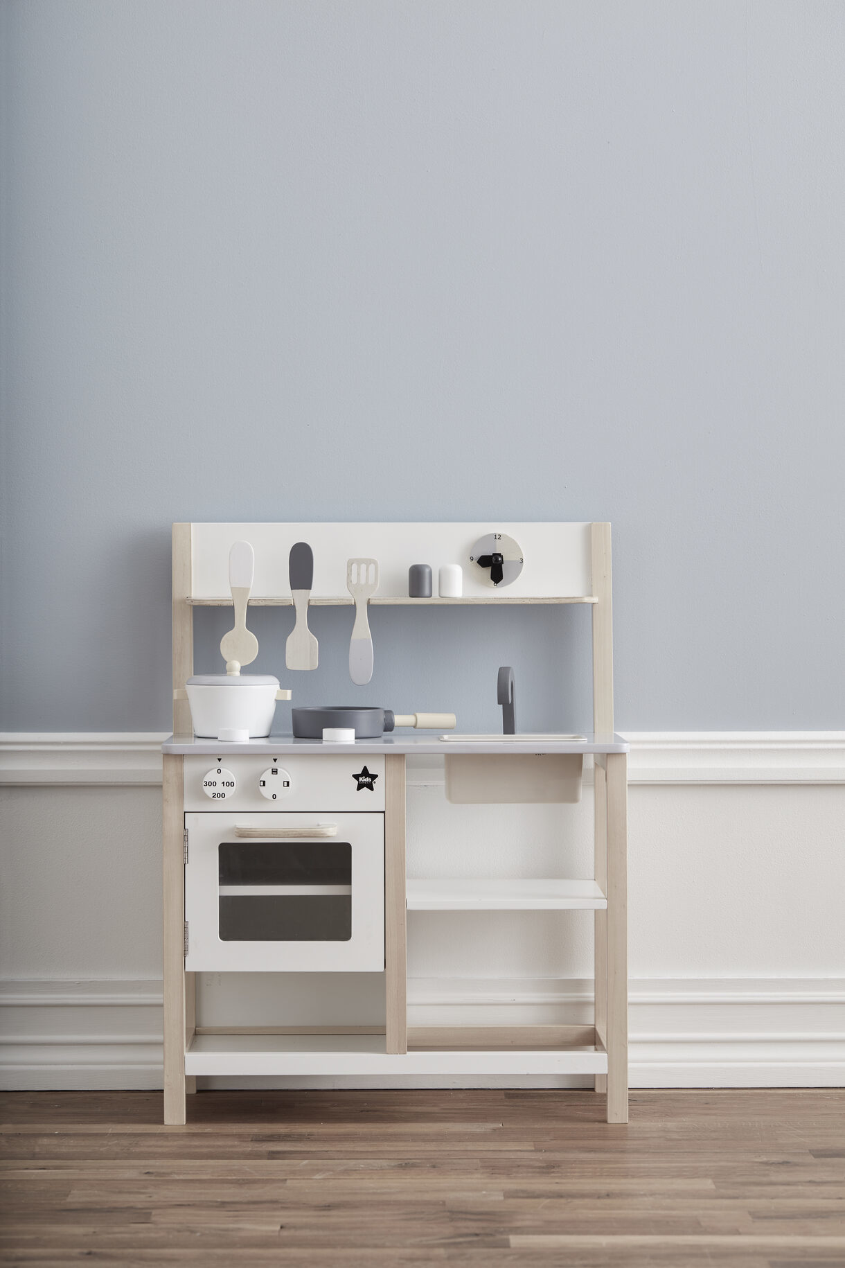 Holzspielküche mit Kochutensilien, Spüle und Ofen vor hellblauer Wand.