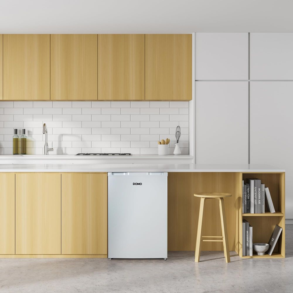 Un mini frigorifero bianco DOMO si trova tra mobili in legno chiaro in una cucina moderna.