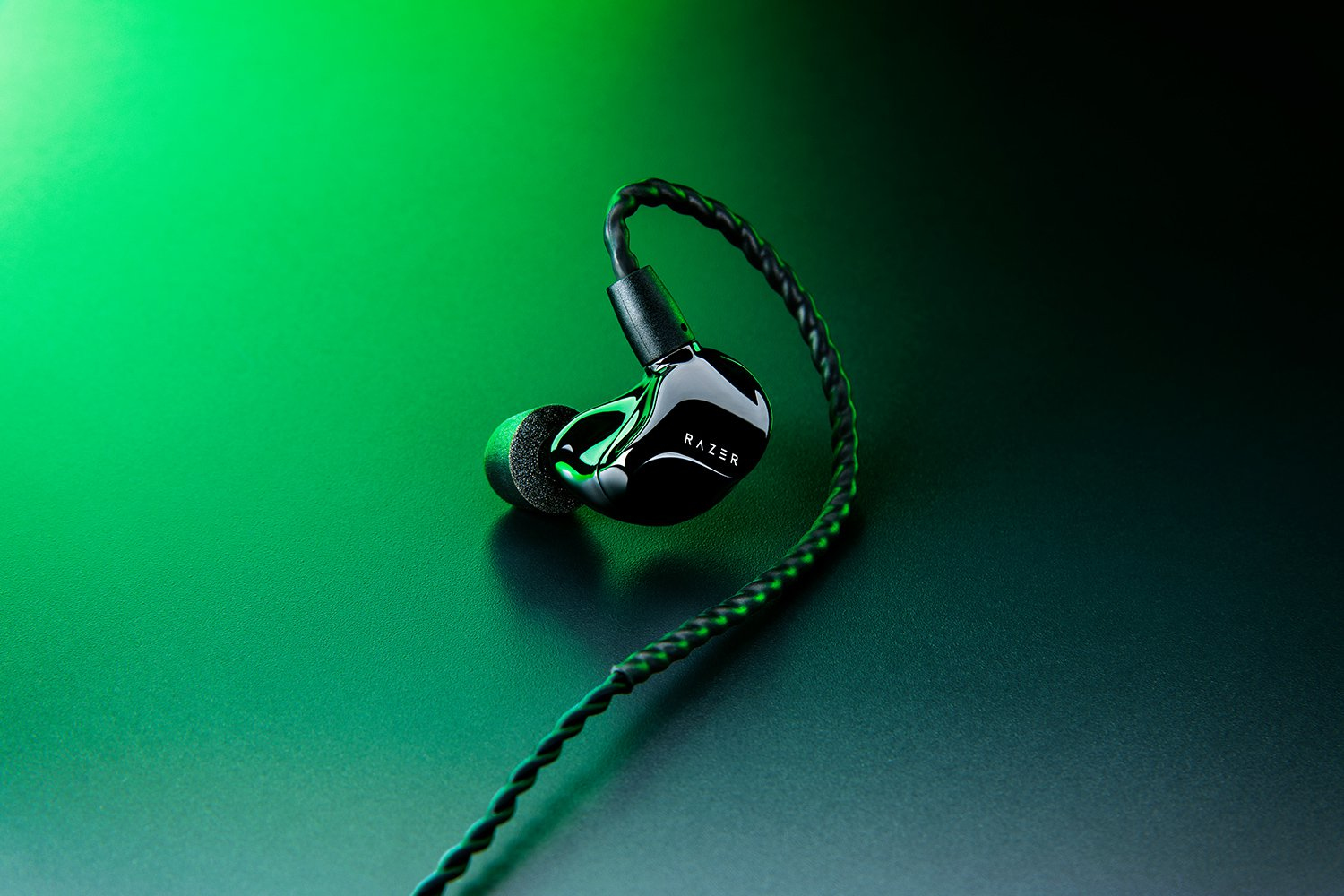 Un auricolare Razer nero con cavo intrecciato su superficie scura con illuminazione verde.