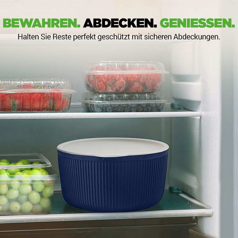Ein dunkler Vorratsbehälter mit weißem Deckel steht in einem Kühlschrank neben Obst.