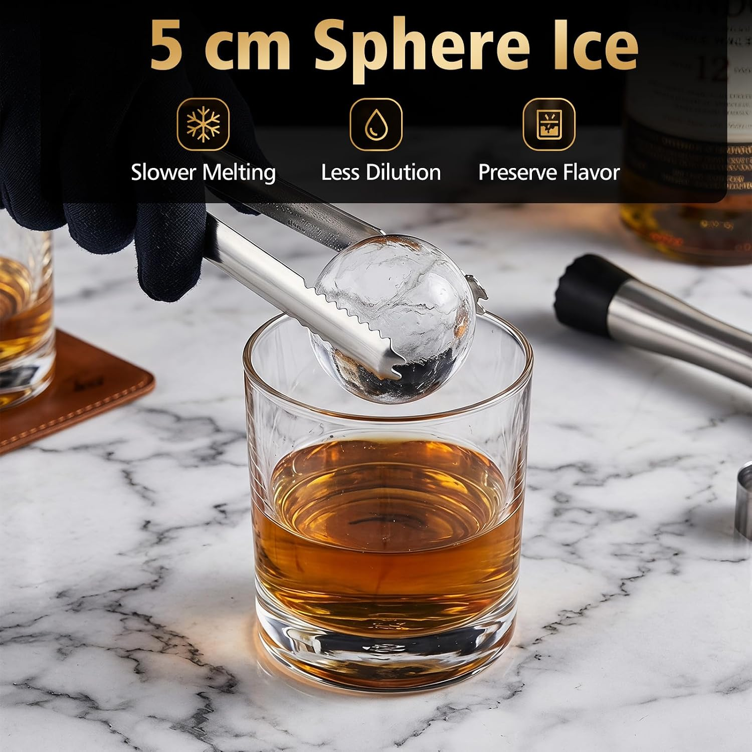Ein Glas Whisky mit einem Eisball, der mit einer Zange gehalten wird.