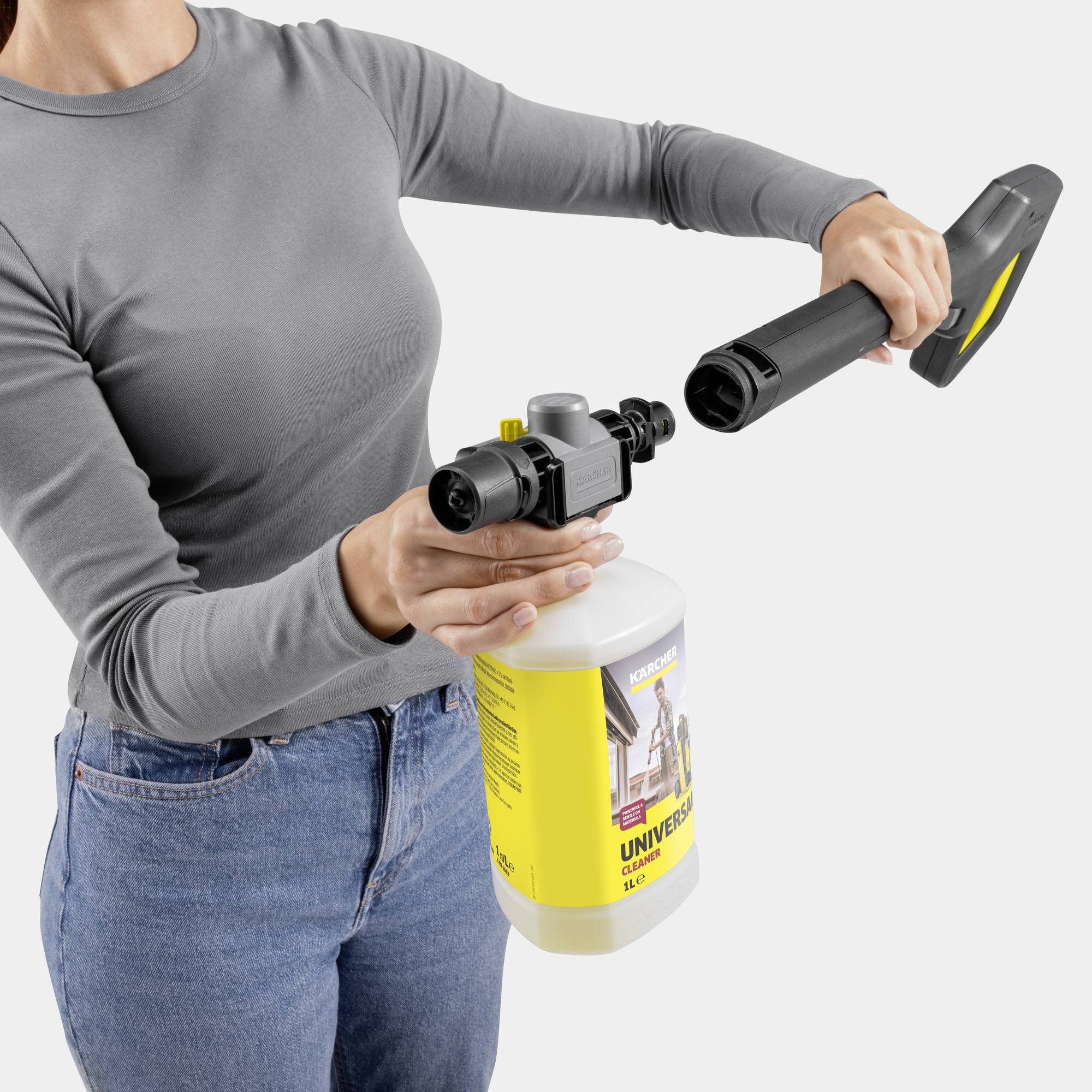 Persona in jeans e maglia grigia monta lancia idropulitrice e flacone detergente.