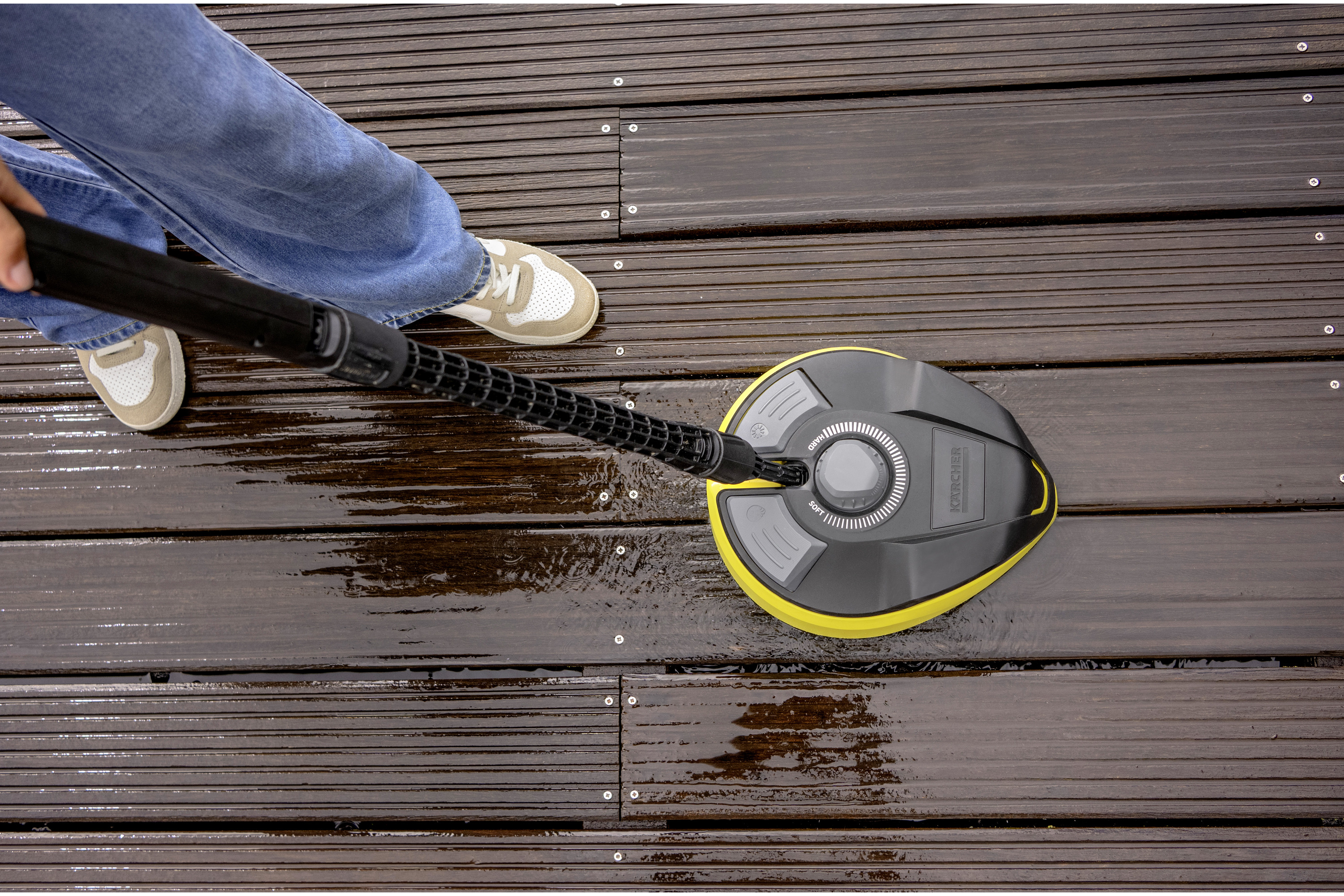 Persona pulisce assi di legno marroni con idropulitrice gialla e nera.