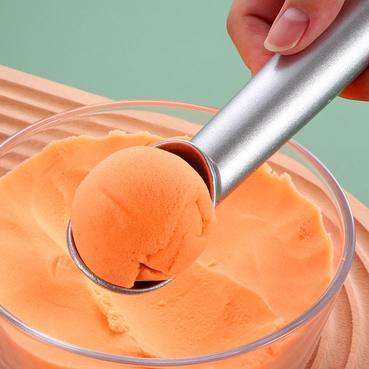 Eine Hand benutzt einen silbernen Löffel, um ein Eis aus einer Schüssel zu schöpfen.