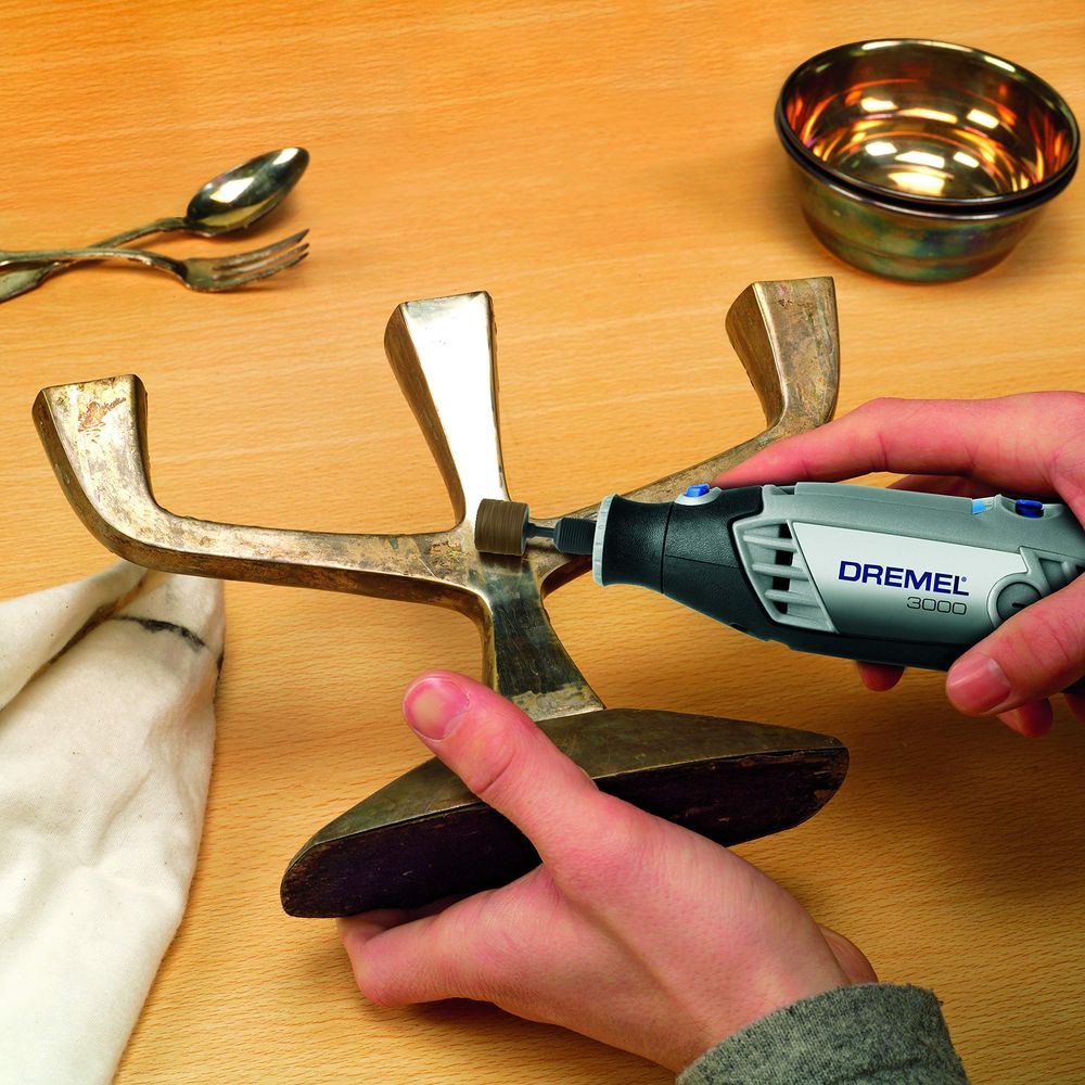 Eine Hand hält ein Dremel-Werkzeug und reinigt ein Bronzestück.