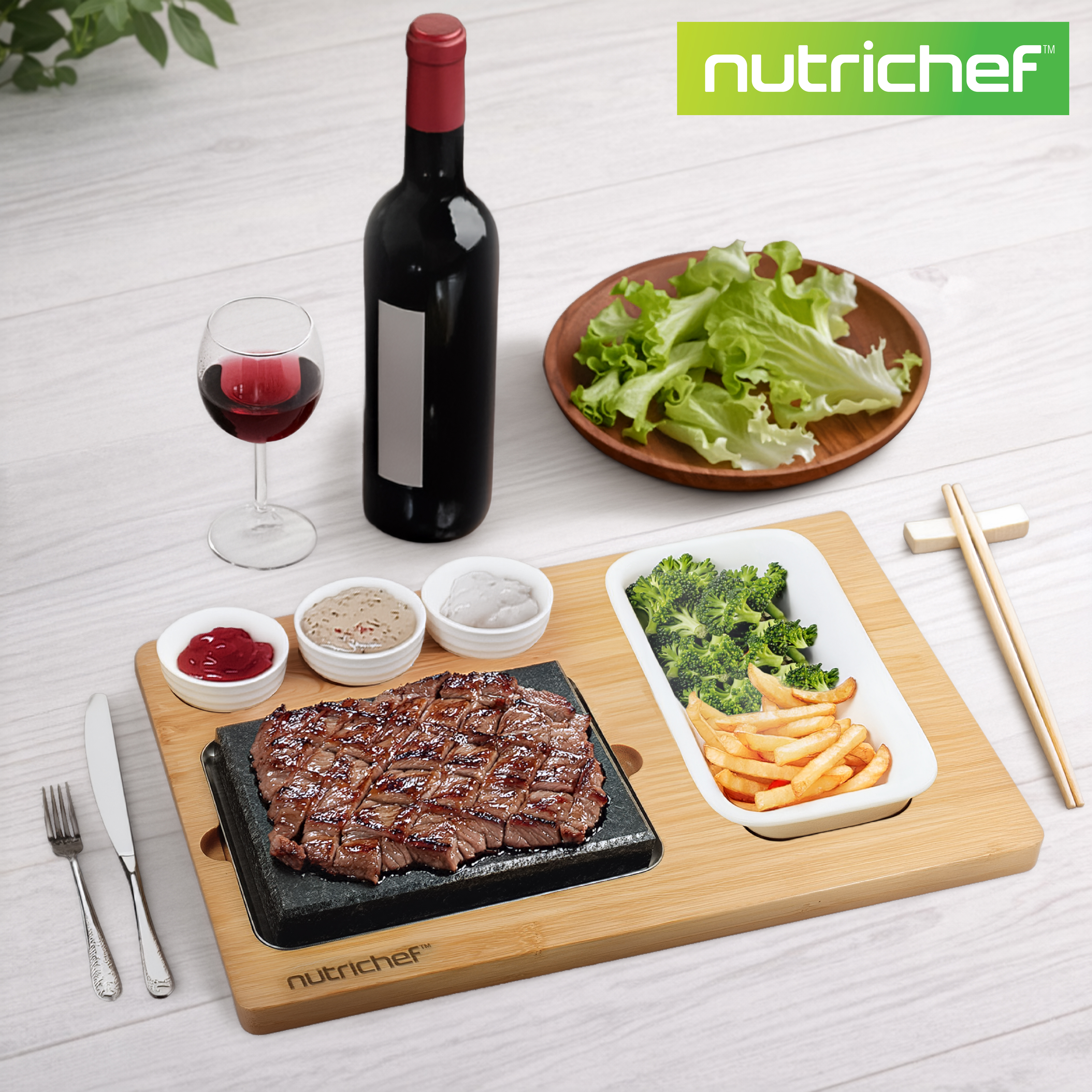 Ein gegrilltes Steak mit Beilagen, Wein und Salat auf einem Holztisch.