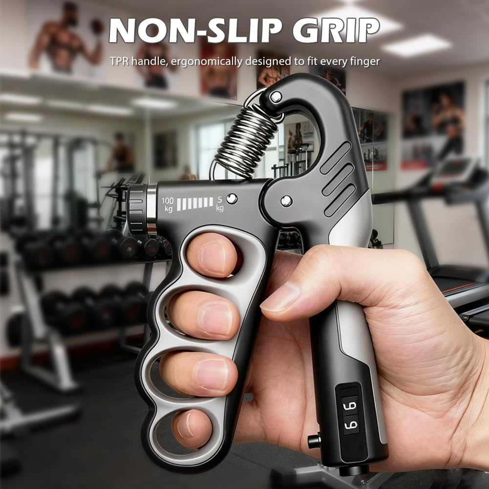 Grauer Handtrainer mit Zählwerk, in einer Hand gehalten, Fitnessstudio im Hintergrund.