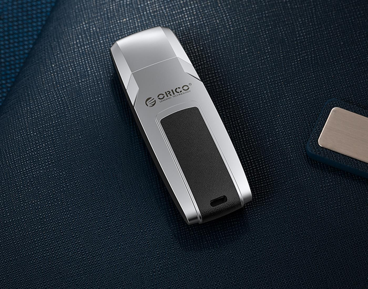 Siyah ek parçalı gümüş USB bellek, koyu mavi kumaş üzerinde duruyor.