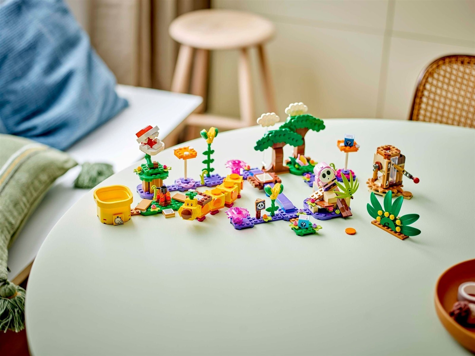 Scène colorée de jouets Lego avec chenille jaune, arbre et personnages sur une table.