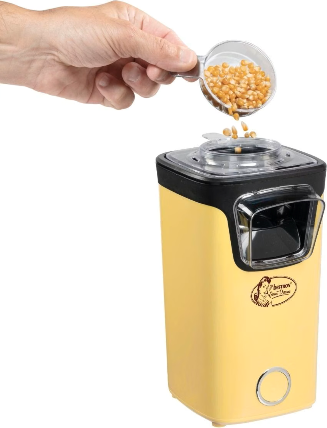 Una mano rovescia una paletta di chicchi di mais in una macchina per popcorn gialla.