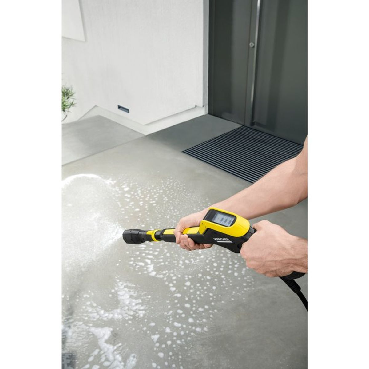 Persona pulisce pavimento con idropulitrice. Manico giallo, getto d'acqua.