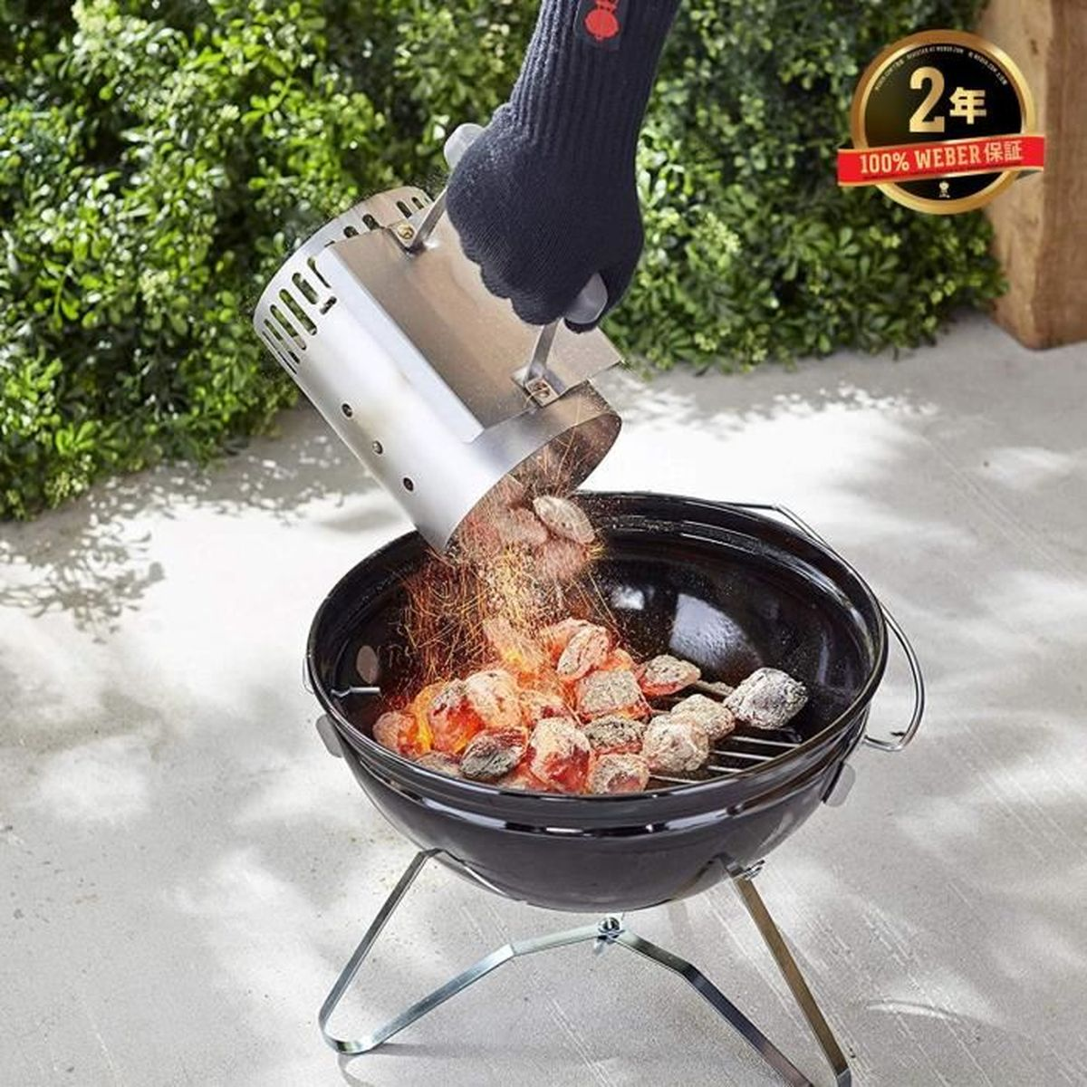 Una mano enguantada vierte brasas calientes de un encendedor de chimenea en una parrilla.
