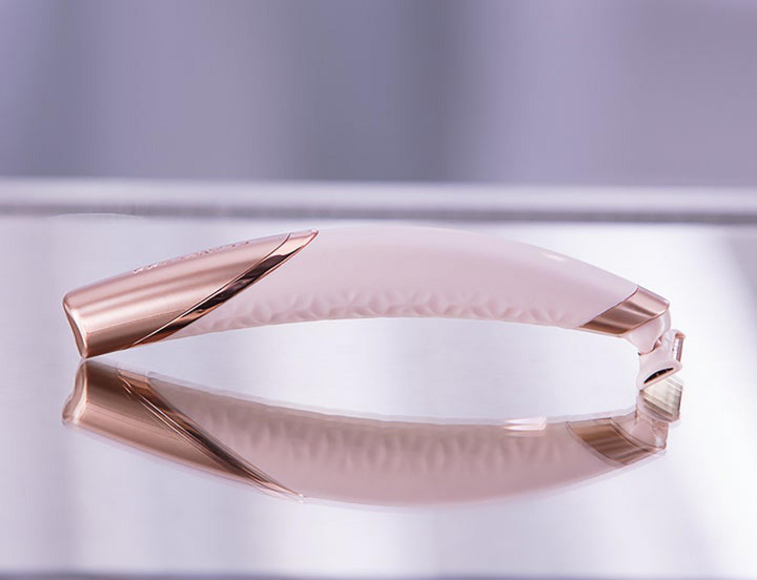 Una piastra per capelli color oro rosa e crema con riflesso su una superficie liscia.