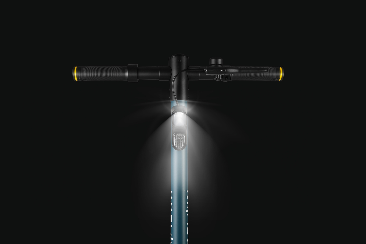 Vista frontale di uno scooter elettrico con manubrio, luce e sfondo scuro.