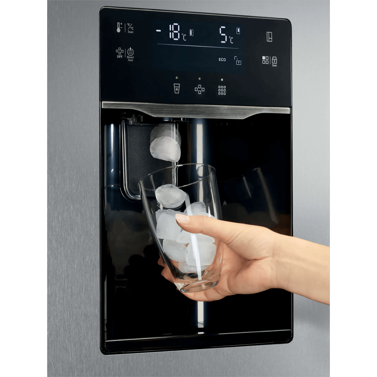 Una mano llena cubitos de hielo en un vaso bajo un dispensador de agua de refrigerador.