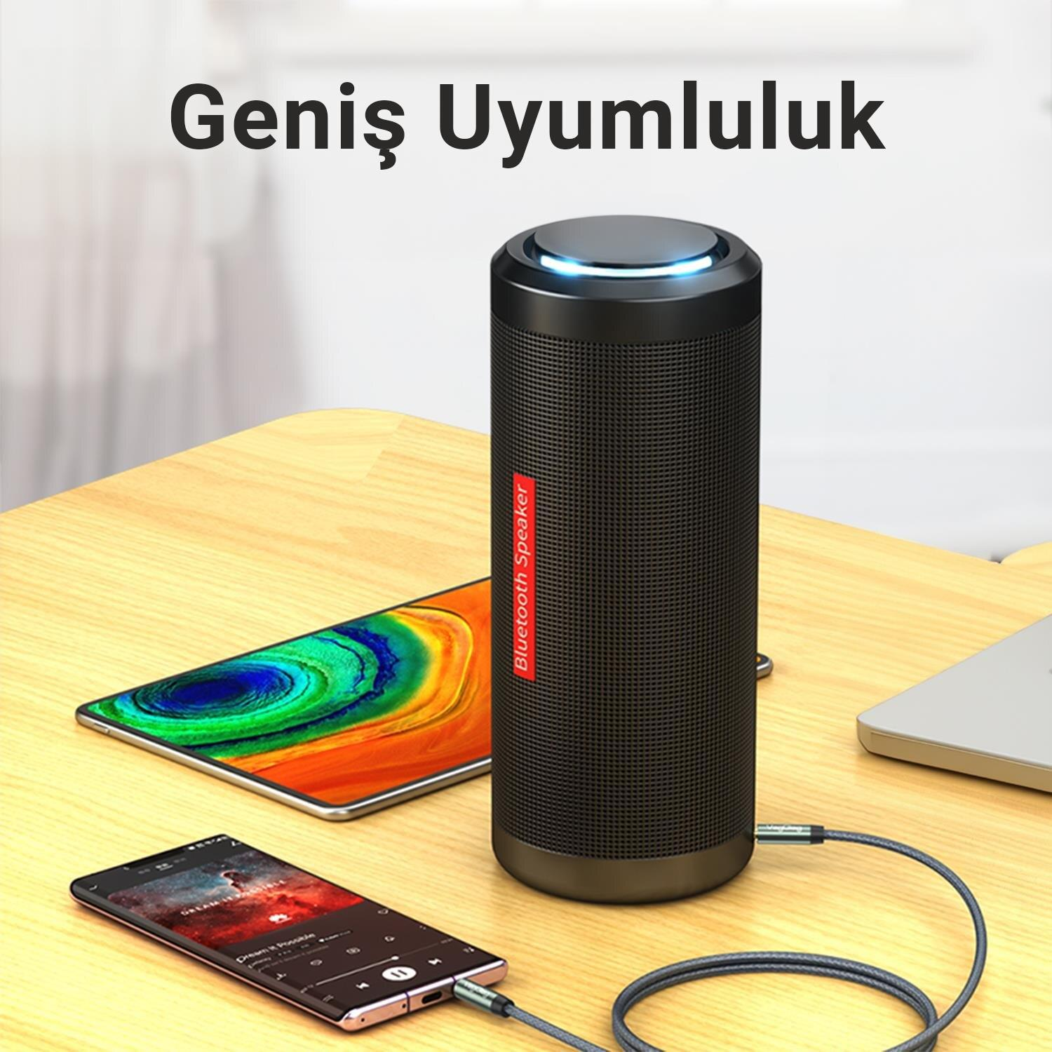 Telefona kabloyla bağlı siyah Bluetooth hoparlör, yanında telefon ve laptop.