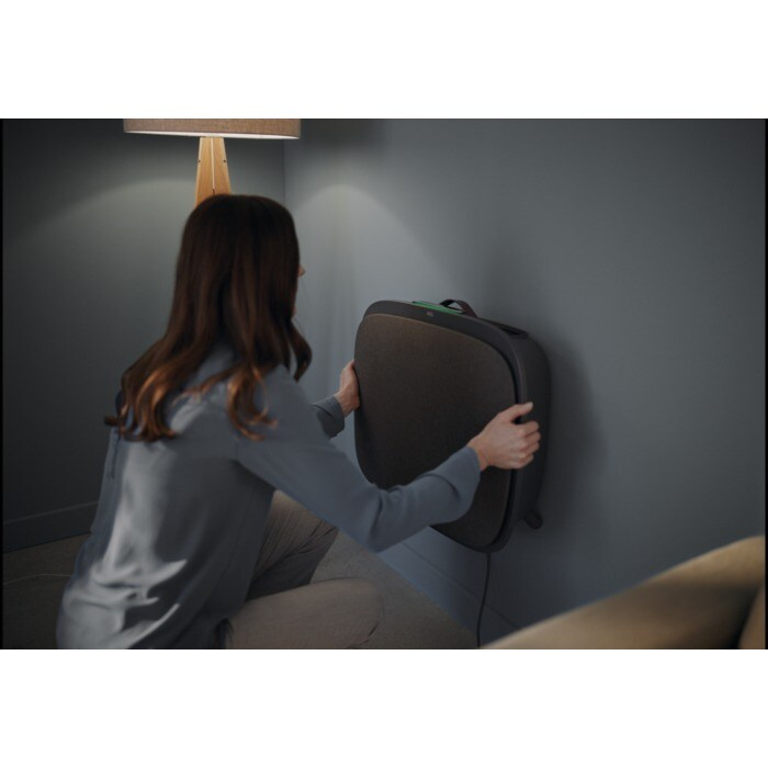 Una mujer cuelga un dispositivo rectangular oscuro en una pared gris.